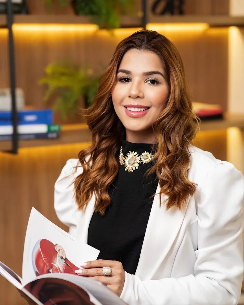Dentista da Odonto Harmonie de blazer branco segurando um livro no consultório